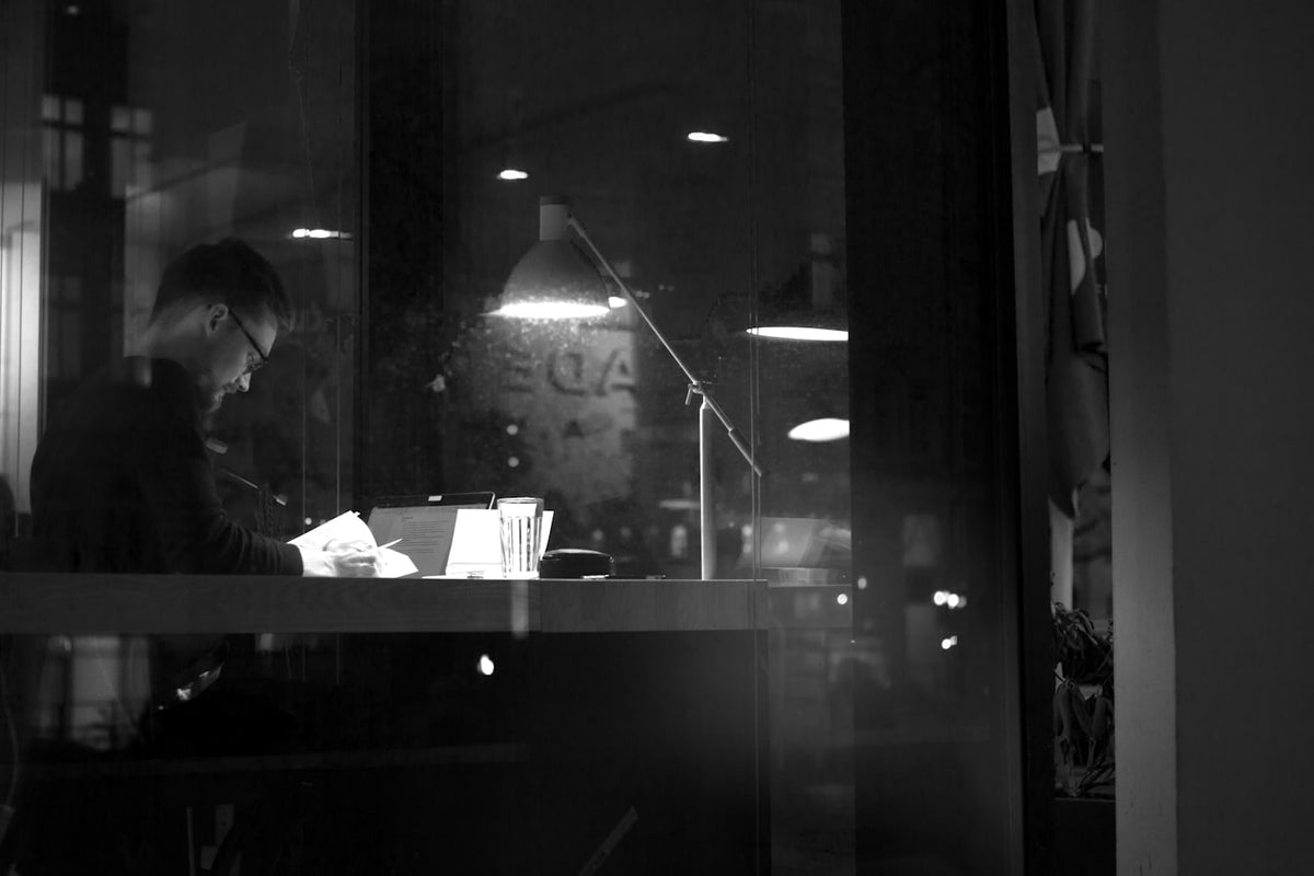 Student studying alone at a desk by a window at night, focused on laptop