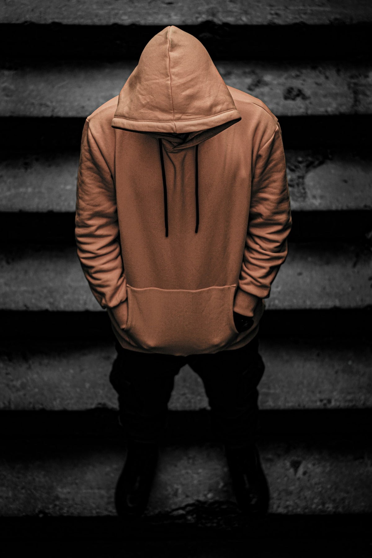 Student in an oversized brown hoodie and black trousers standing on a dim stairwell