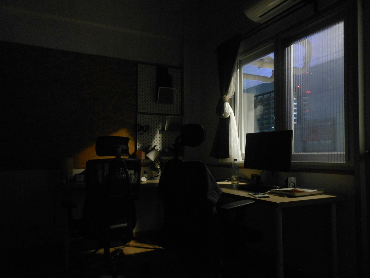 Person working alone at a desk in a dark room, screen illuminating the space