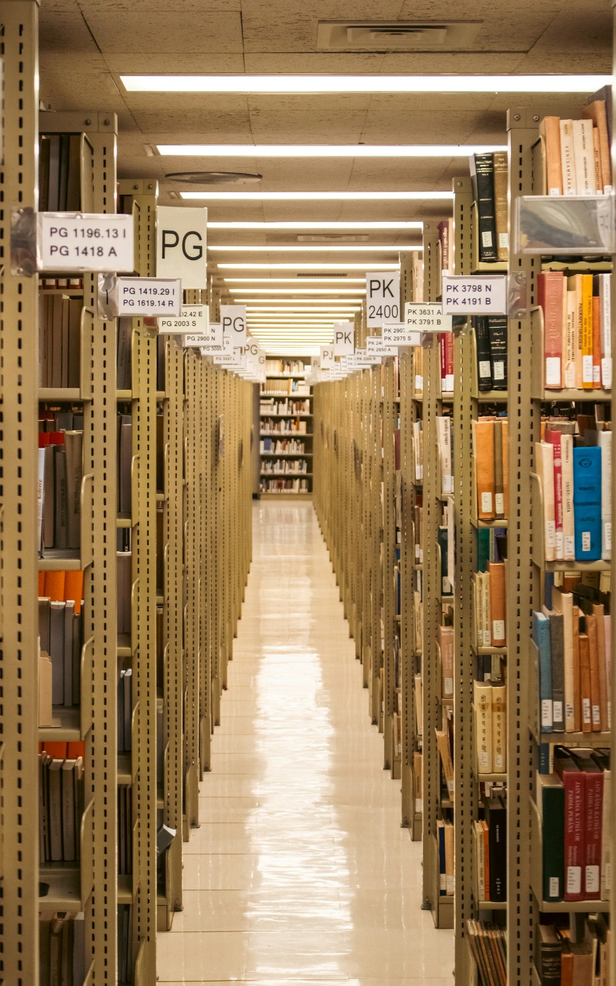 A long, dimly lit university library aisle lined with tall bookshelves