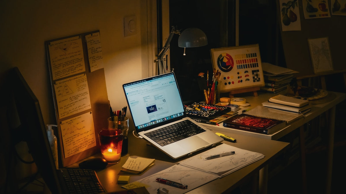 Desk with laptop, books, and a lit candle at night