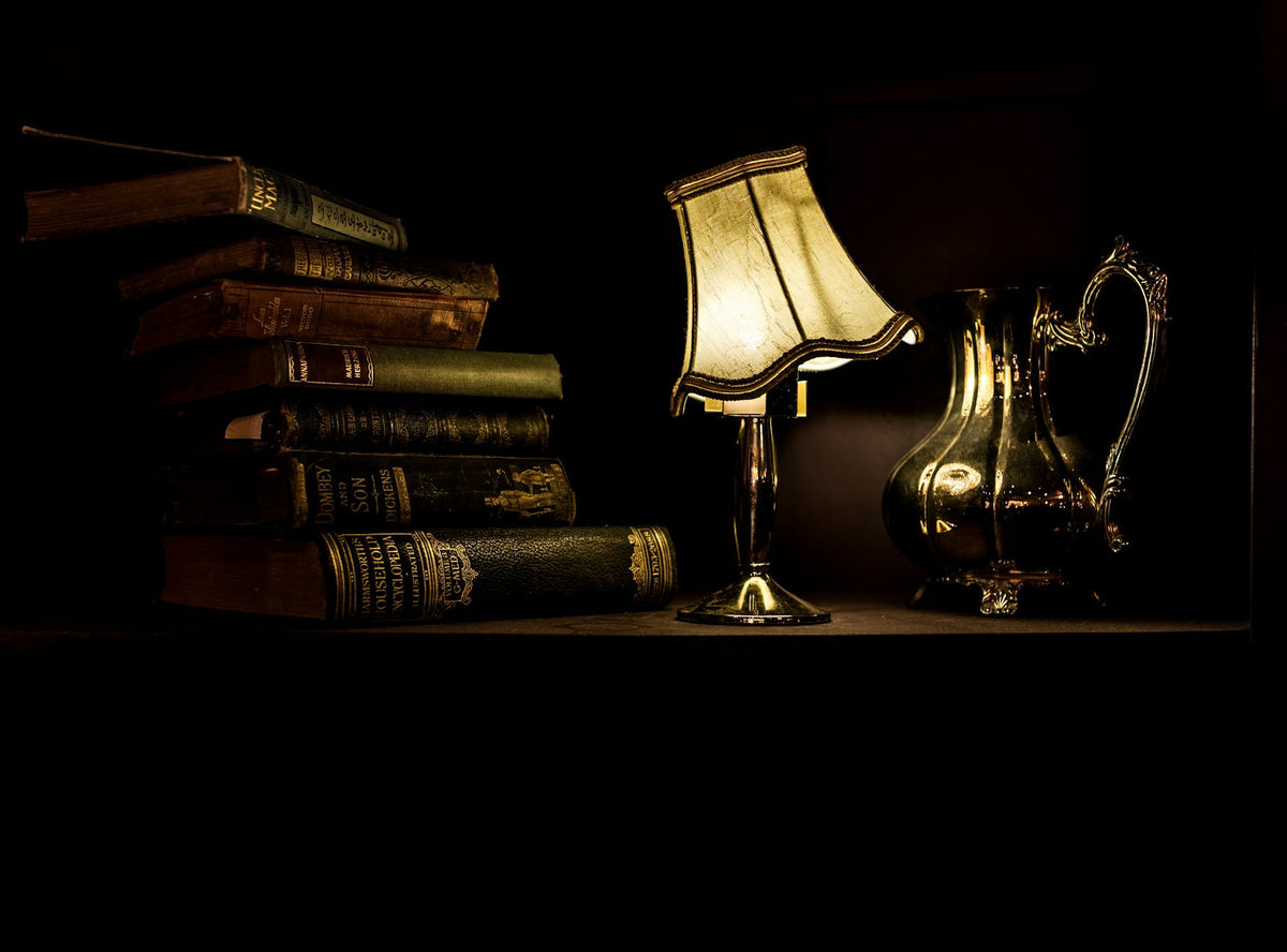 A desk lamp glowing over a pile of books at night