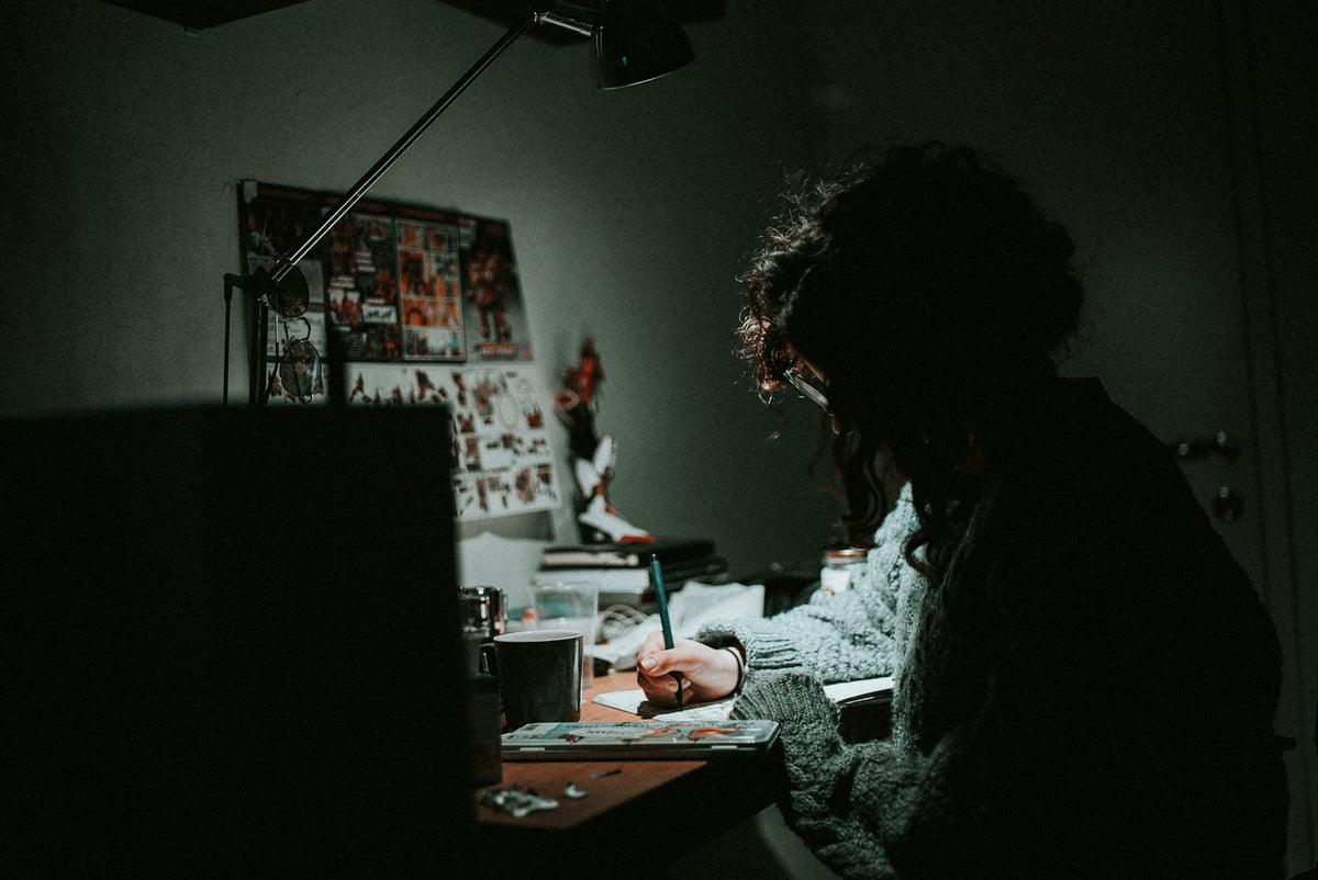 Low light photo of a student in a knit sweatshirt writing at a desk at night
