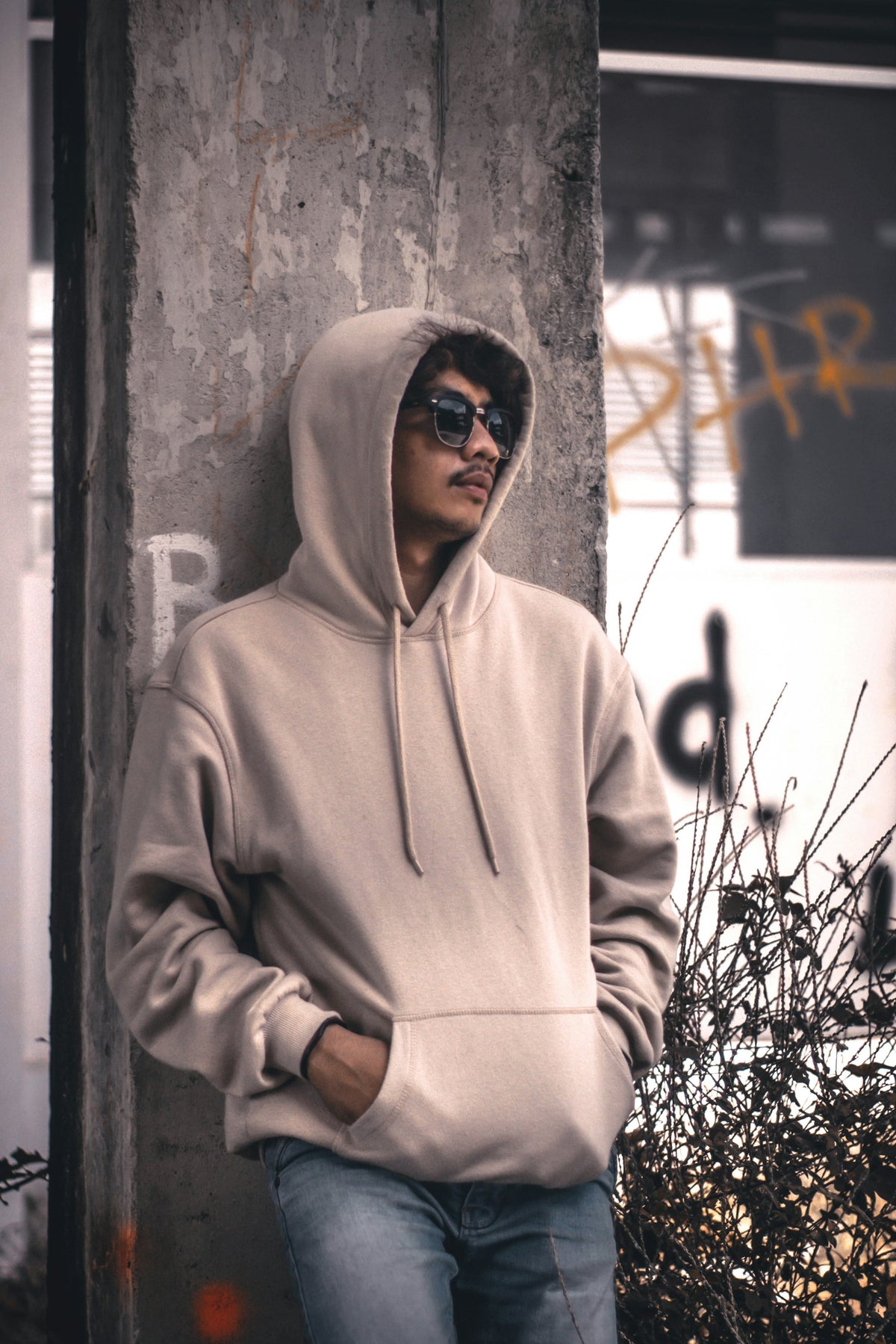 Person in an oversized grey hoodie leaning casually against a wall