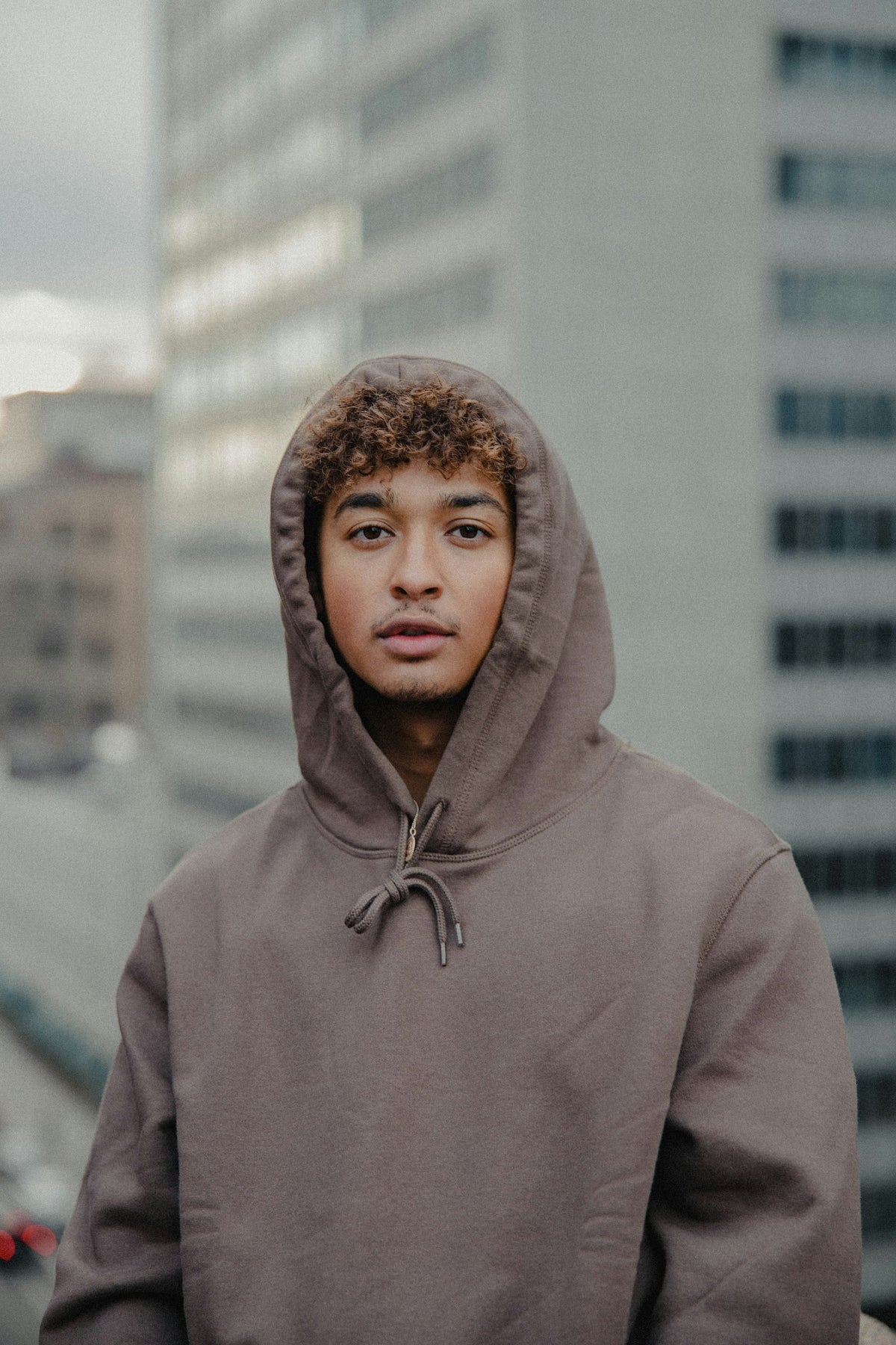 Man in a grey hoodie standing against a white wall in clean natural light