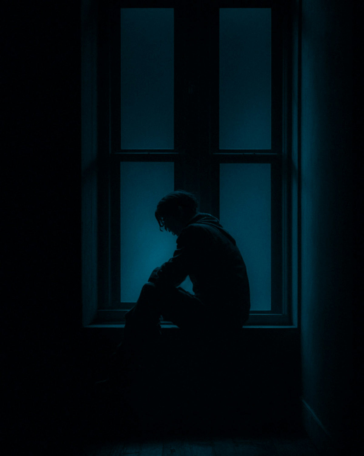 A person sitting in the dark by a window at night, waiting