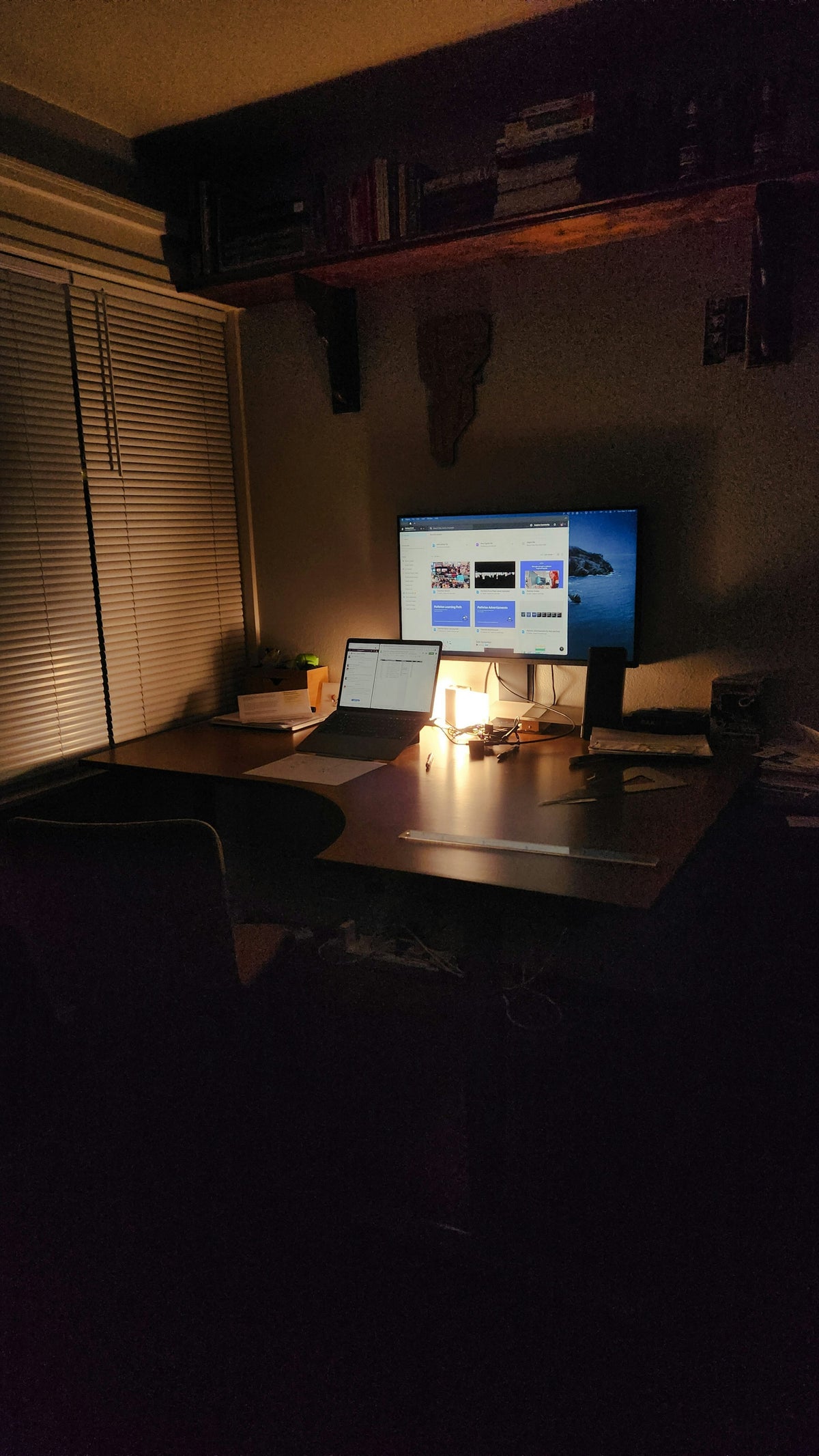 A cozy nighttime workspace with a laptop, warm desk lamp glow, and shelves of books