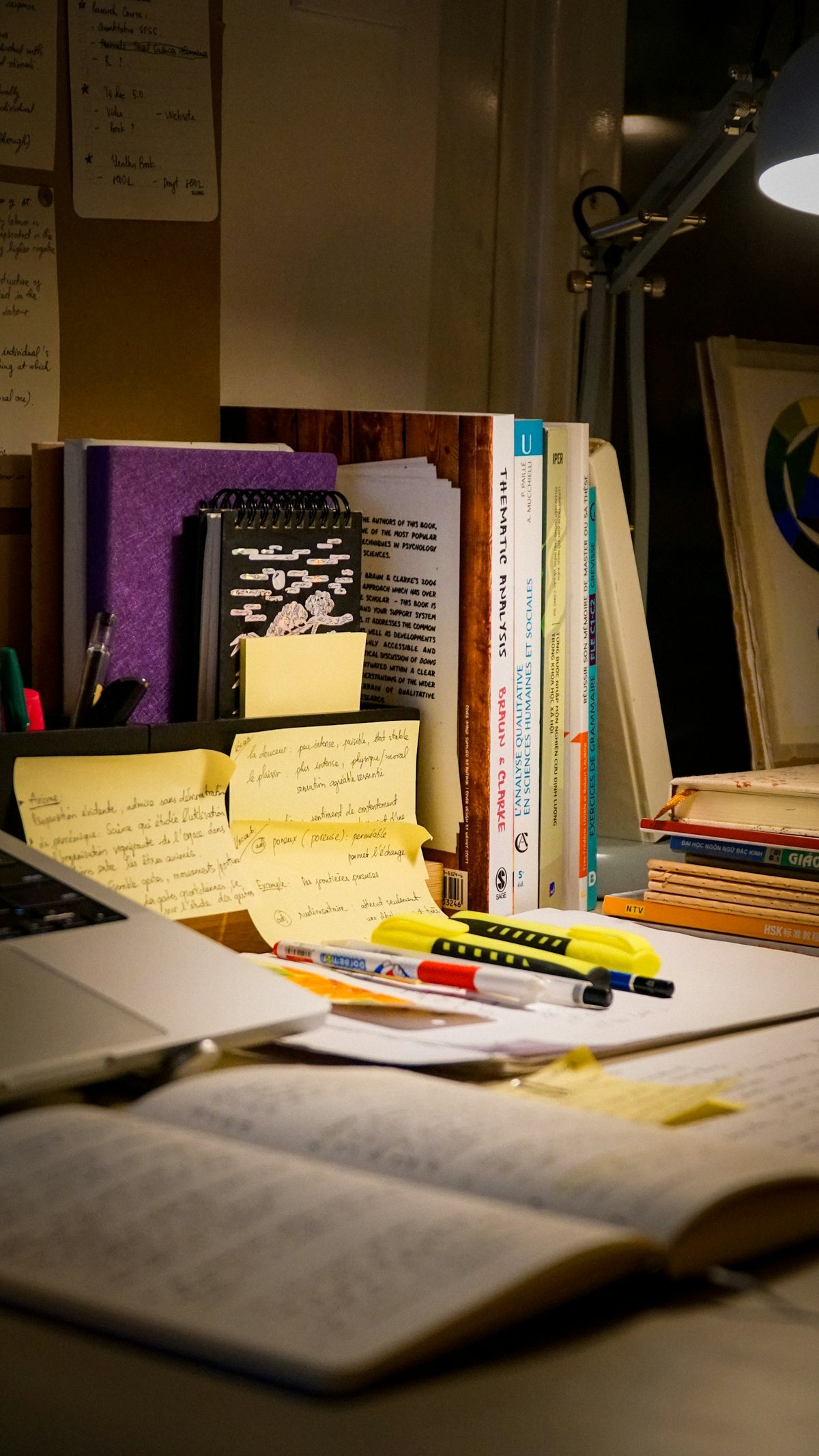 A cozy late-night study desk with an open book, laptop, and handwritten notes under lamp light